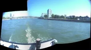 Panoramic stitched view combining rear camera frames showing the vessel wake, river channel, and bridge.